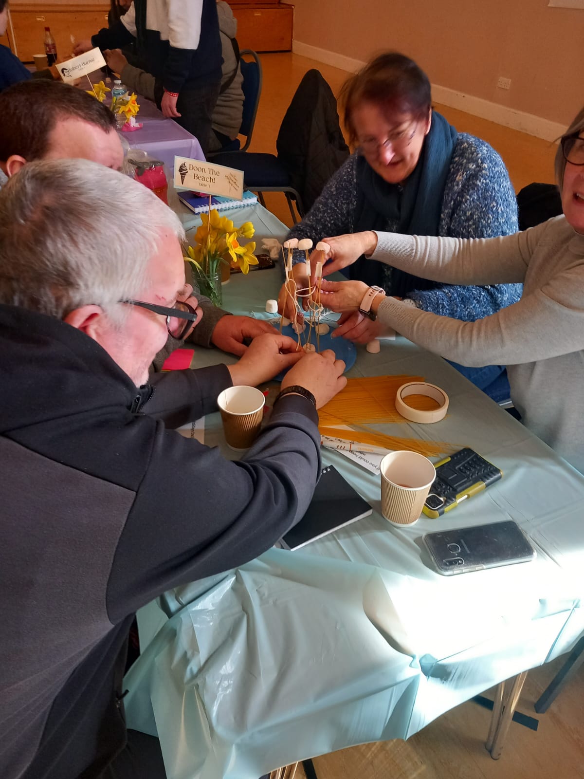 Members work together to create a tower out of dried spaghetti, marshmallows and tape.